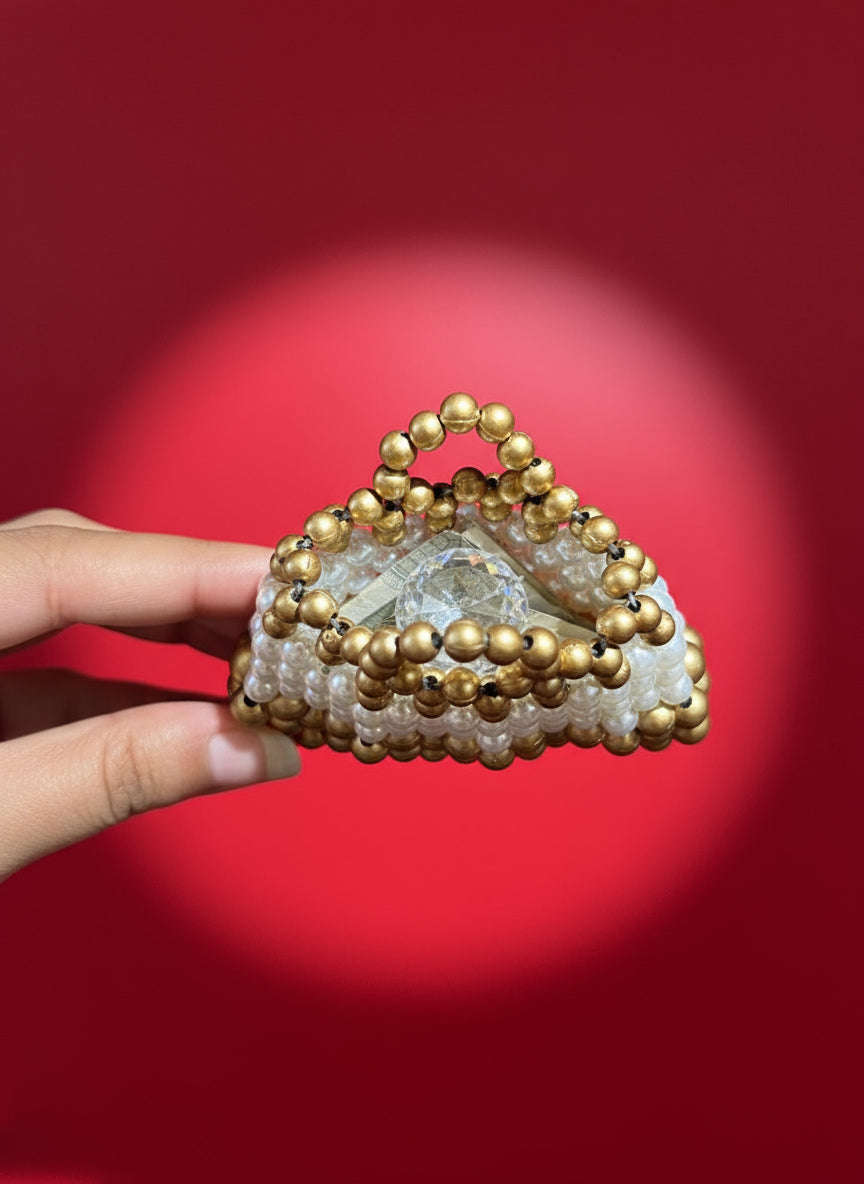 Triangular mirror with gold bead border held by a hand on a wooden surface